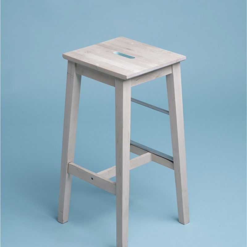 A single white stool against a soft blue wall